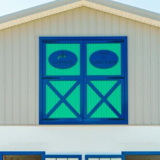 Blue and green sliding loft doors on a building. Features include custom finish and protective stall grill options.