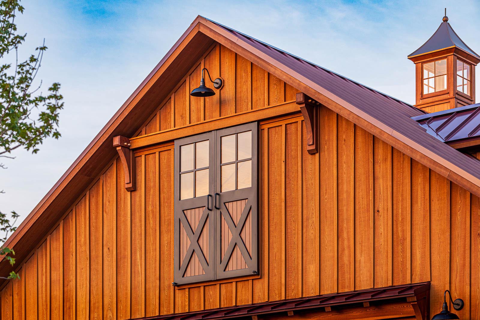 Wooden barn with sliding loft doors in rustic finish under a clear sky.