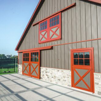 Gray barn with red sliding loft and barn doors and Dutch windows, featuring stone accents. Includes entry door with grill.