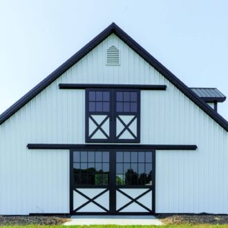 Modern barn with black and white sliding loft and exterior doors, featuring crossbuck design and large windows.