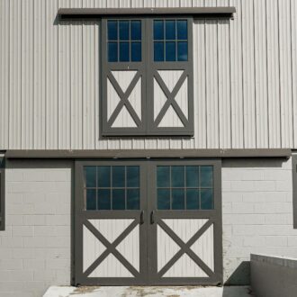 Dual sliding barn doors and hay loft doors with crossbuck design, gray finish, textured siding, and matching window panels.