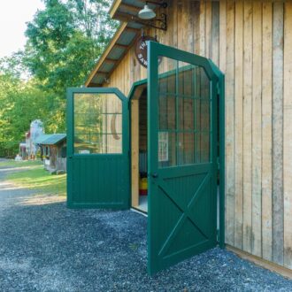 Green carriage door with glass panes on wooden exterior, showcasing entry doors with color and finish options.
