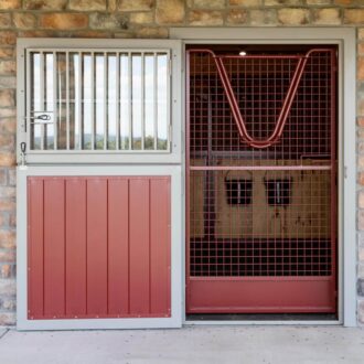 Dutch door with protective stall grill, red finish, set in stone wall. Ideal for barns and stables, customizable options.
