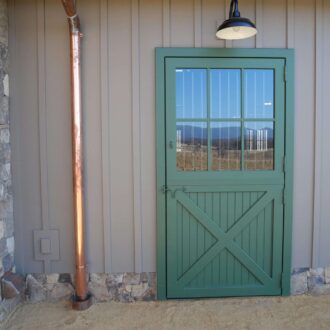 Green Dutch entry door with glass panels against stone and wood wall, showing finish options and mountain view.