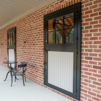 Dutch doors with protective stall grills on brick wall, featuring black finish and white paneling. Outdoor seating visible.