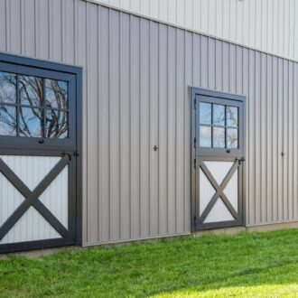 Exterior view of three black-framed Dutch doors on a beige building, showcasing sleek design and functional cross-braces.