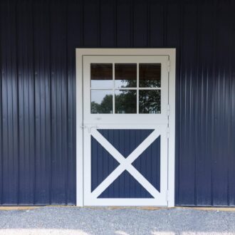 White Dutch door with window panes on navy blue metal building, featuring X-brace design. Optional finish and color.