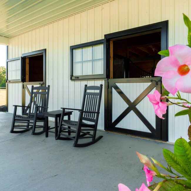 Black Dutch doors with top awning windows on a white barn, featuring optional black finish, flowers, and chairs.
