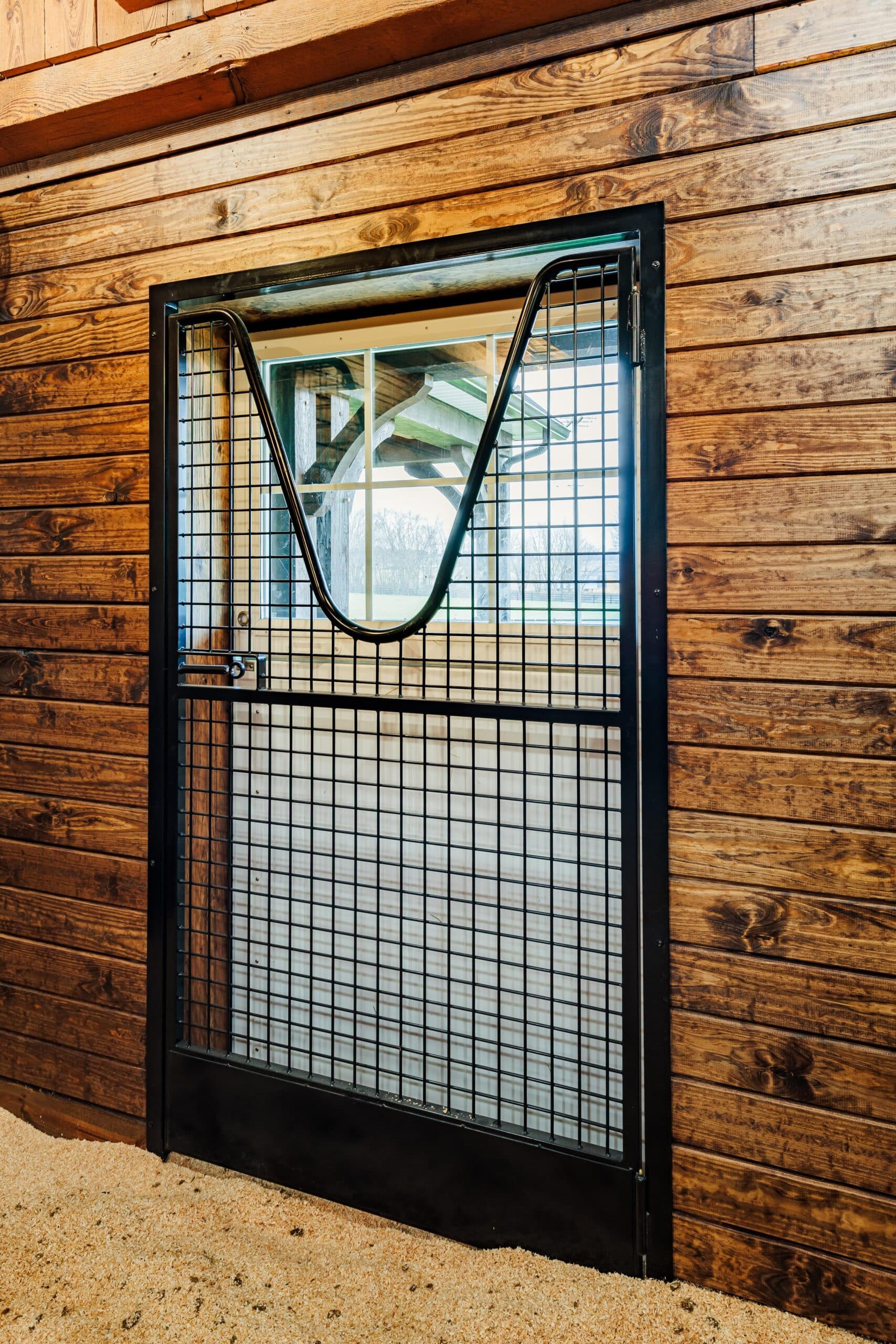 Black mesh dutch door with protective grill set in a wooden frame, showcasing a rustic finish option.