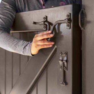 Person opening a dark finish Dutch door with secure latch, showcasing quality hardware in close-up view.