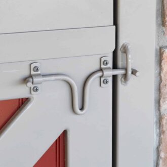 Close-up of gray steel slide latch on red sliding barn door, showcasing custom finish and durable hardware against stone wall backdrop.