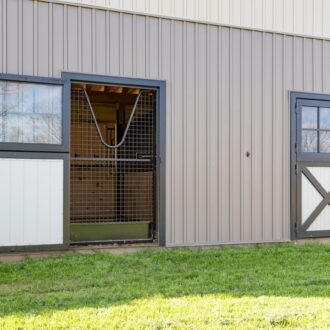 Dutch doors with protective stall grills, featuring black finish and white panels in a barn setting.