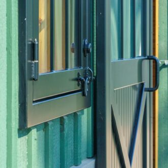 Green sliding barn doors with protective grills and black handles on a green exterior.