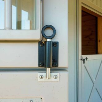 Close-up of beige Dutch door with protective grill and black spring latch hardware, showcasing durable finish for barn entry.