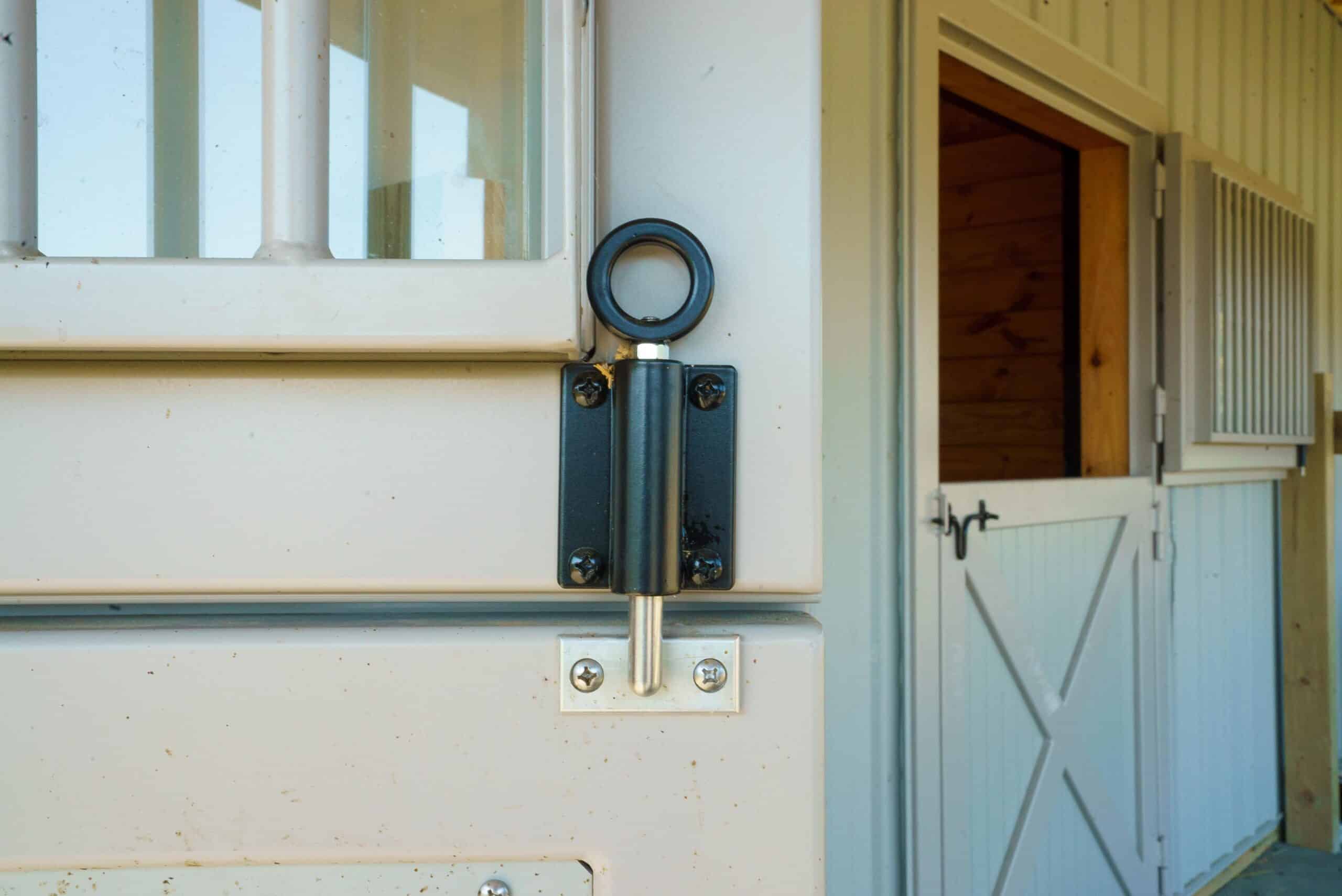 Close-up of beige Dutch door with protective grill and black spring latch hardware, showcasing durable finish for barn entry.