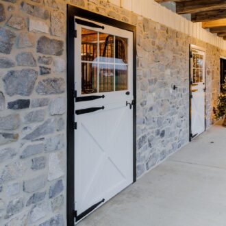 White Dutch door with black trim in a stone wall, featuring stall grill and holiday decor. Ideal for barn settings.