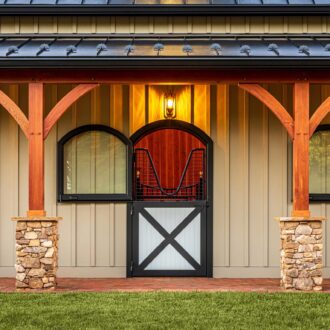 Elegant barn facade with arch-topped Dutch doors, mesh protective grills. Warm finish, stone accents, evening lights.