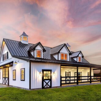 Elegant barn with black sliding barn doors, Dutch doors, protective grills, and custom finish under a vibrant sunset sky.