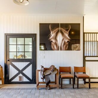 Barn with black Dutch door, horse photo, saddles, and protective stall grills, showcasing custom equestrian design.