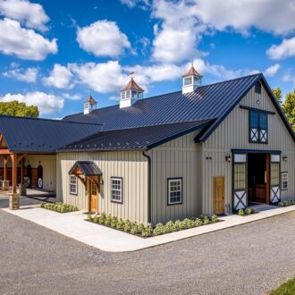 Beautiful barn with black roof featuring sliding barn doors, Dutch doors, carriage doors, awning windows; lush landscape.