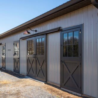 Stylish barn with dark sliding barn doors, featuring mesh grills and elegant finish against a sunny rural backdrop.