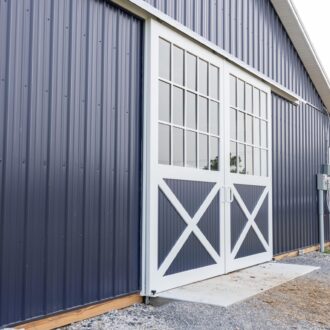 Sliding barn doors with white frame and glass panels on blue siding. Custom finish options available.