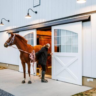 A woman walking a horse out of a barn
