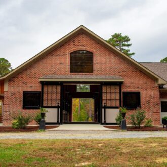 Brick building with large sliding barn doors. Surrounded by greenery and a gravel path.