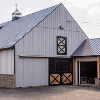 Gray barn with black sliding barn doors featuring a wooden cross pattern and a Dutch window.