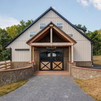 Front view of a barn featuring sliding carriage doors, entry doors, and awning windows. Wooden and stone finish.