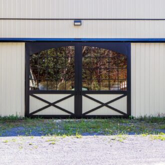 Sliding barn doors with black frame, grid glass panels on beige wall. Features include X-pattern and finish options.