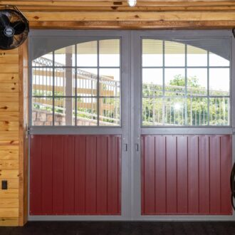 Barn interior with split sliding barn doors, featuring protective stall grills and a burgundy finish.