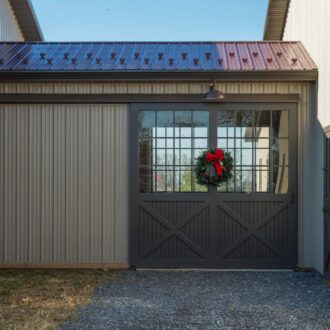 Barn with gray sliding exterior barn doors adorned with a festive wreath; features metal roofing and matching Dutch doors.