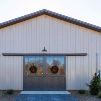 Gray sliding barn doors with windows and wreaths on a beige building, highlighting custom finish options.