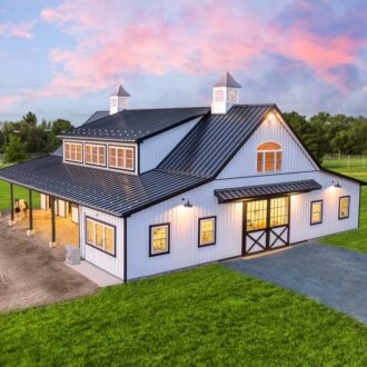 White barn with a black metal roof against a sunset backdrop.
