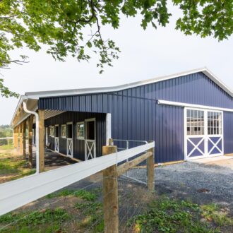 Blue barn with sliding barn doors, mesh windows, and white trim, offering customizable finish options and colors.