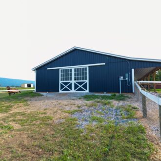 Blue barn with white sliding exterior barn doors, showcasing protective stall grills and mesh in a rural setting.