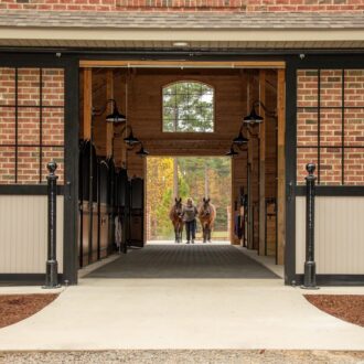 Elegant brick barn with black-framed sliding barn doors, featuring protective stall grills and modern design.