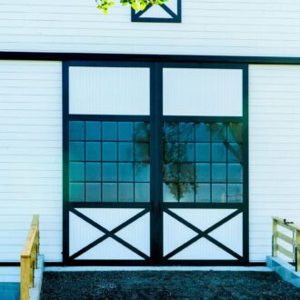 Sliding barn doors with black trim and glass panels on a white building, standard finish options available.
