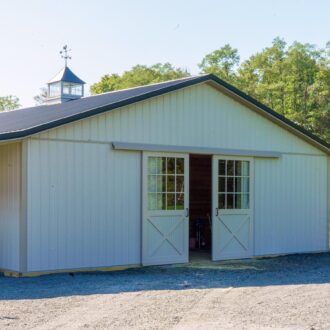 Barn with white sliding barn doors and entry door, featuring glass panels. Surrounded by trees and rural landscape.