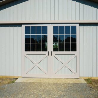 White sliding barn doors with cross design, glass panels; perfect for stables, customizable finishes available.