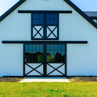 White barn with black sliding barn and carriage doors, featuring window panels. Ideal for rustic and modern styles.