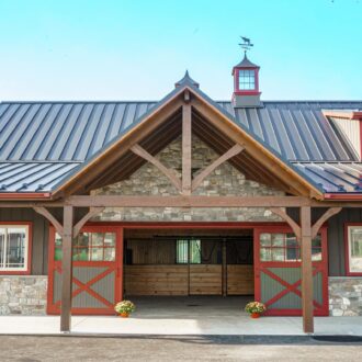 Rustic barn with custom sliding exterior barn doors, protective stall grills, stone accents, and vibrant window trim.