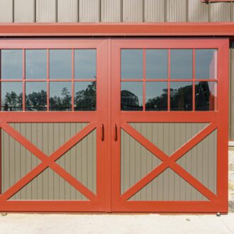 Red sliding barn doors with glass panes and X-pattern wood paneling in tan finish. Ideal for versatile entry.