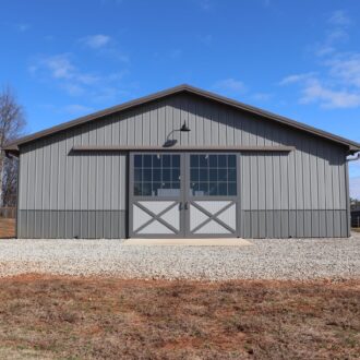 Gray barn with sliding exterior barn doors, featuring glass panels and a gable roof, under a clear blue sky.