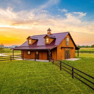 A modern brown horse barn with fencing