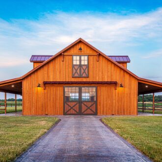 Rustic barn with sliding loft doors, carriage doors, and Dutch windows, showcasing custom powder coated faux wood finish and outdoor lighting.
