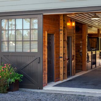 Sliding barn door with window panes, wood finish, and flower accents, entering a stable with protective stall grills.