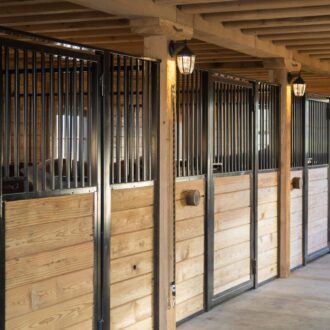 Wooden horse stalls with protective grill panels in a barn, featuring customizable finish and color options.