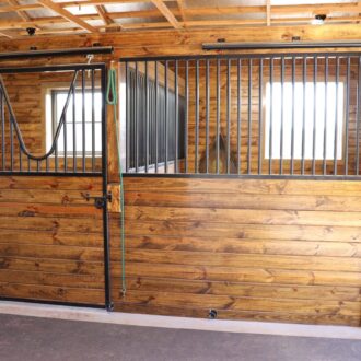 Wooden sliding barn doors with protective stall grills in a bright stable, showcasing a rustic finish.